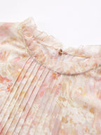 Close-up of a 100% mulberry silk blouse featuring a ruffled stand collar, delicate floral print, and fine pleating details.