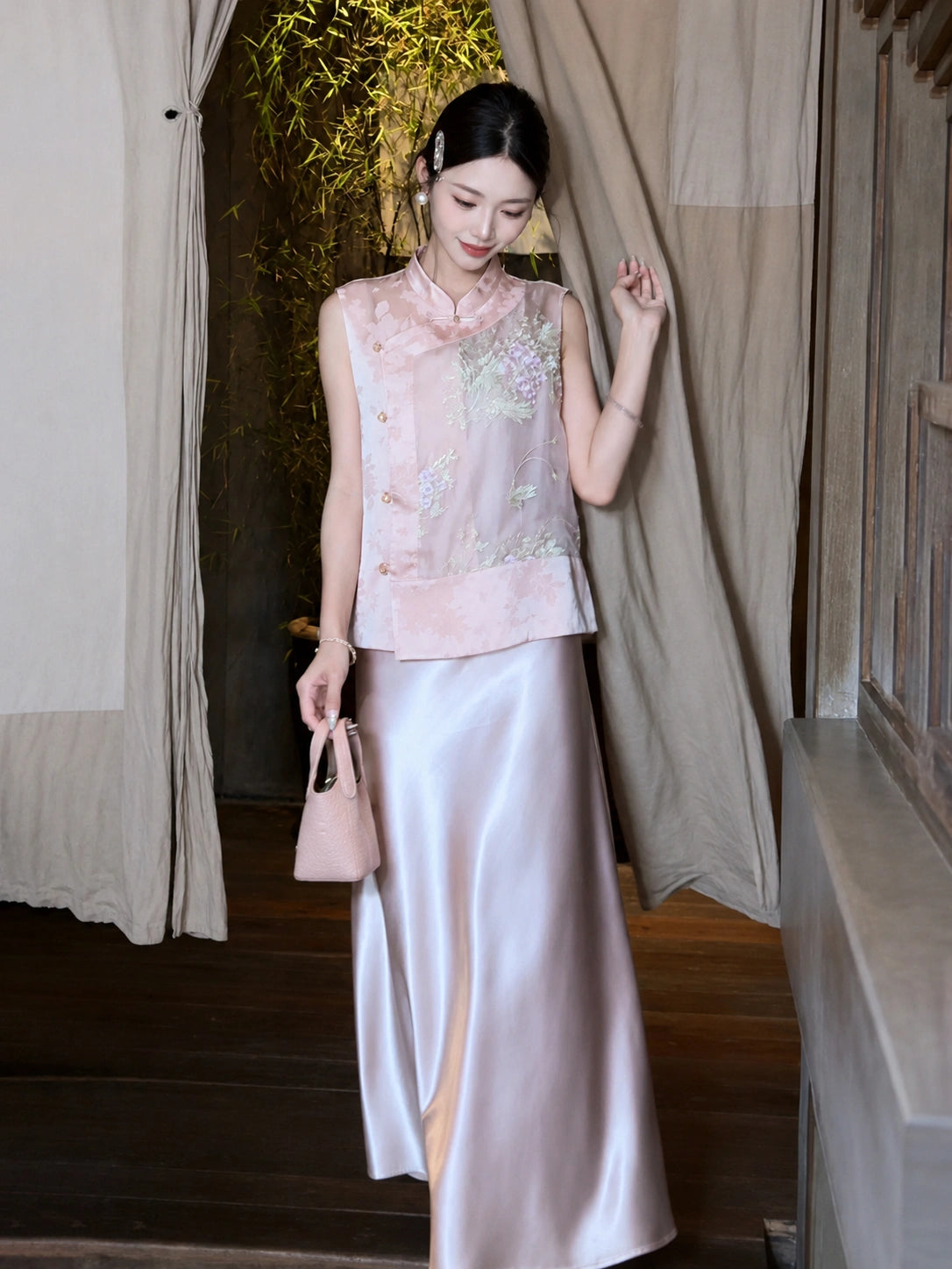 Model wearing a pink satin maxi skirt paired with a matching embroidered Cheongsam top, holding a pink handbag.