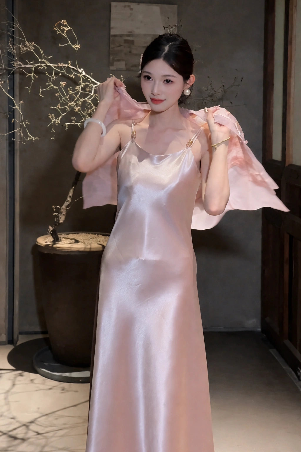 Model wearing a pink satin slip dress with a matching sheer jacket over her shoulders, featuring gold-tone strap hardware, 100% polyester fabric.