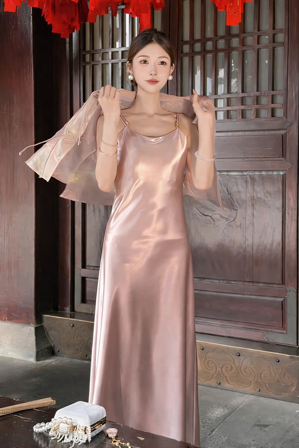 Close-up of a pink satin dress with a sheer pink jacket draped over the shoulders, highlighting the soft drape of the 100% polyester fabric.