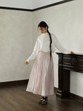 Styling image of a pink glossy high-waist A-line skirt with a white blouse, suitable for daily commuter wear.