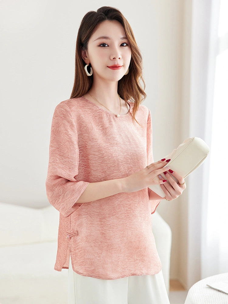 Model wearing a pink silk-blend New Chinese style blouse with a round neckline and relaxed fit, holding a white clutch.