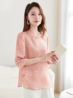 Model wearing a pink silk-blend New Chinese style blouse with a round neckline and relaxed fit, holding a white clutch.