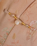 Close-up of a handmade frog closure with gold thread and a pearl-style accent on blush pink silk
