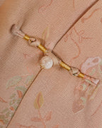 Close-up of a handmade frog closure with gold thread and a pearl-style accent on blush pink silk
