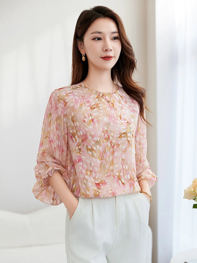 Model in a pink and gold abstract silk blouse, looking to the side, highlighting the elegant drape and lantern sleeve design.