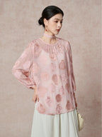 Model wearing a pink sheer silk blouse with an ancient pottery cutwork pattern and a matching necktie, paired with a cream skirt.