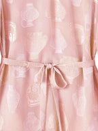 Close-up of a pink 100% mulberry silk blouse showing the sheer chiffon texture, white/silver cutwork vase pattern, and a matching silk tie belt.