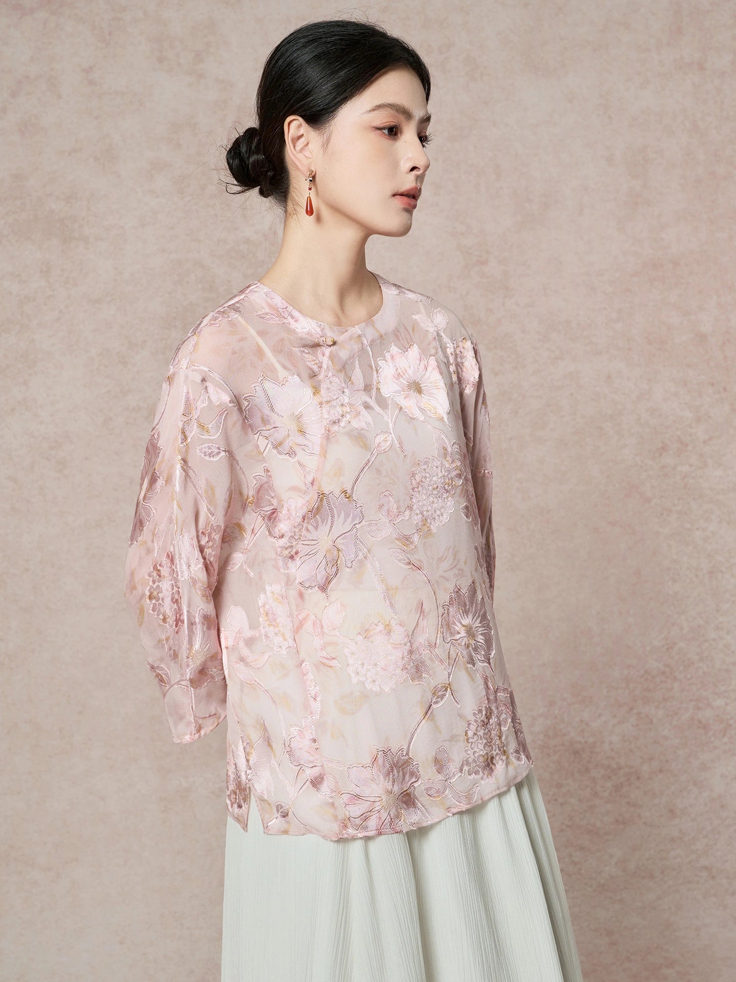 Front view of a pink 100% silk blouse with a round neckline and delicate floral embroidery, styled with a light green pleated skirt for a New Chinese look.