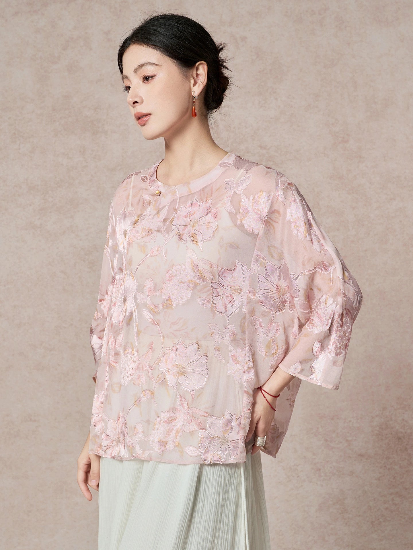 Side view of a pink silk top with a round neckline, highlighting the flowing drape and elegant cutwork pattern.
