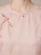 Close-up of the diagonal placket on a pink 93.8% mulberry silk blouse, highlighting the decorative gold and pink buttons and the subtle sheen of the jacquard fabric.
