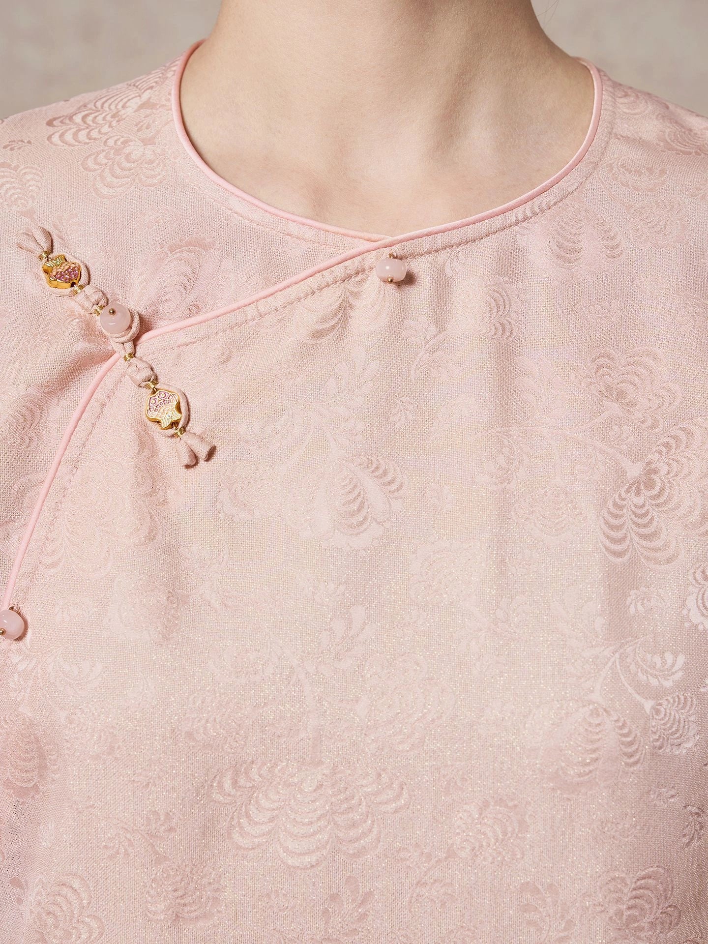 Close-up of the diagonal placket on a pink 93.8% mulberry silk blouse, highlighting the decorative gold and pink buttons and the subtle sheen of the jacquard fabric.