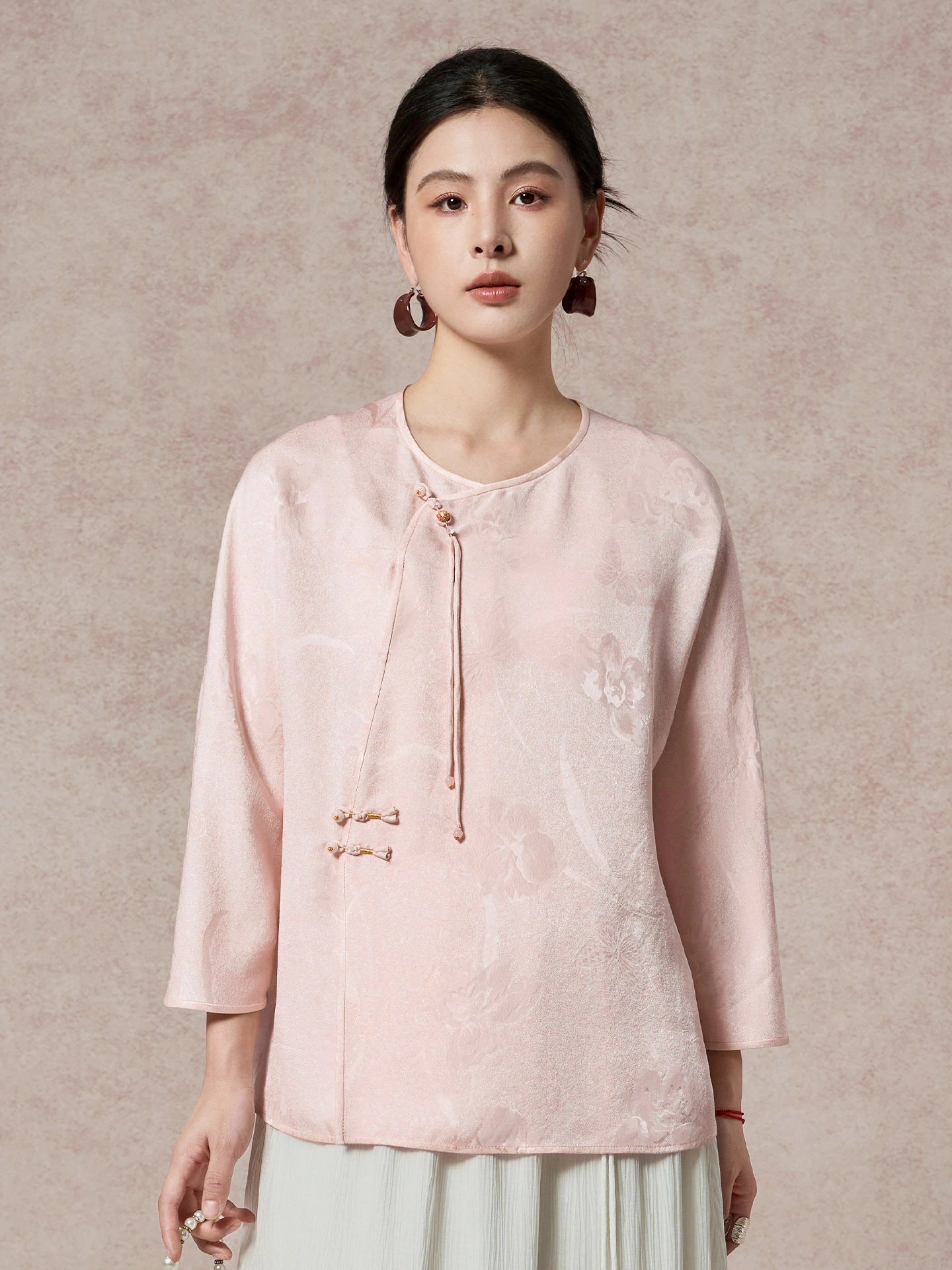 Front view of a women's pink silk blouse with a round neckline and a delicate diagonal placket with decorative tassels and beads.