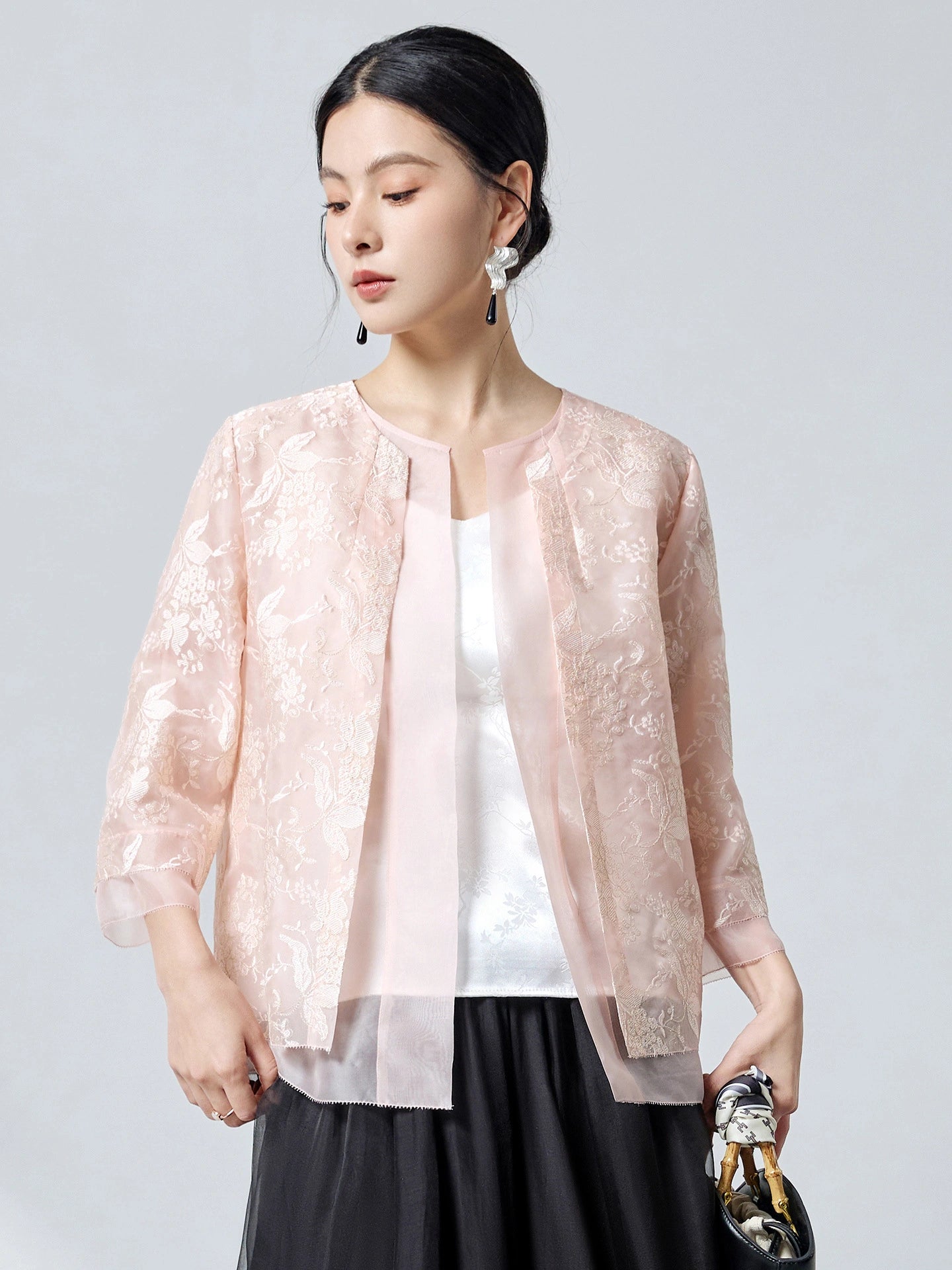 Front view of a pink 100% mulberry silk organza cardigan with open front design and delicate floral embroidery, paired with a black skirt.