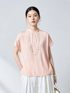 Front view of a pink short-sleeve silk top featuring a stand collar, delicate front pleats, and a relaxed fit, paired with white pleated pants.