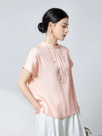 Side view of a pink silk blouse with a stand collar and subtle textured pleats, styled with a long pearl necklace, highlighting the elegant drape and silky sheen.