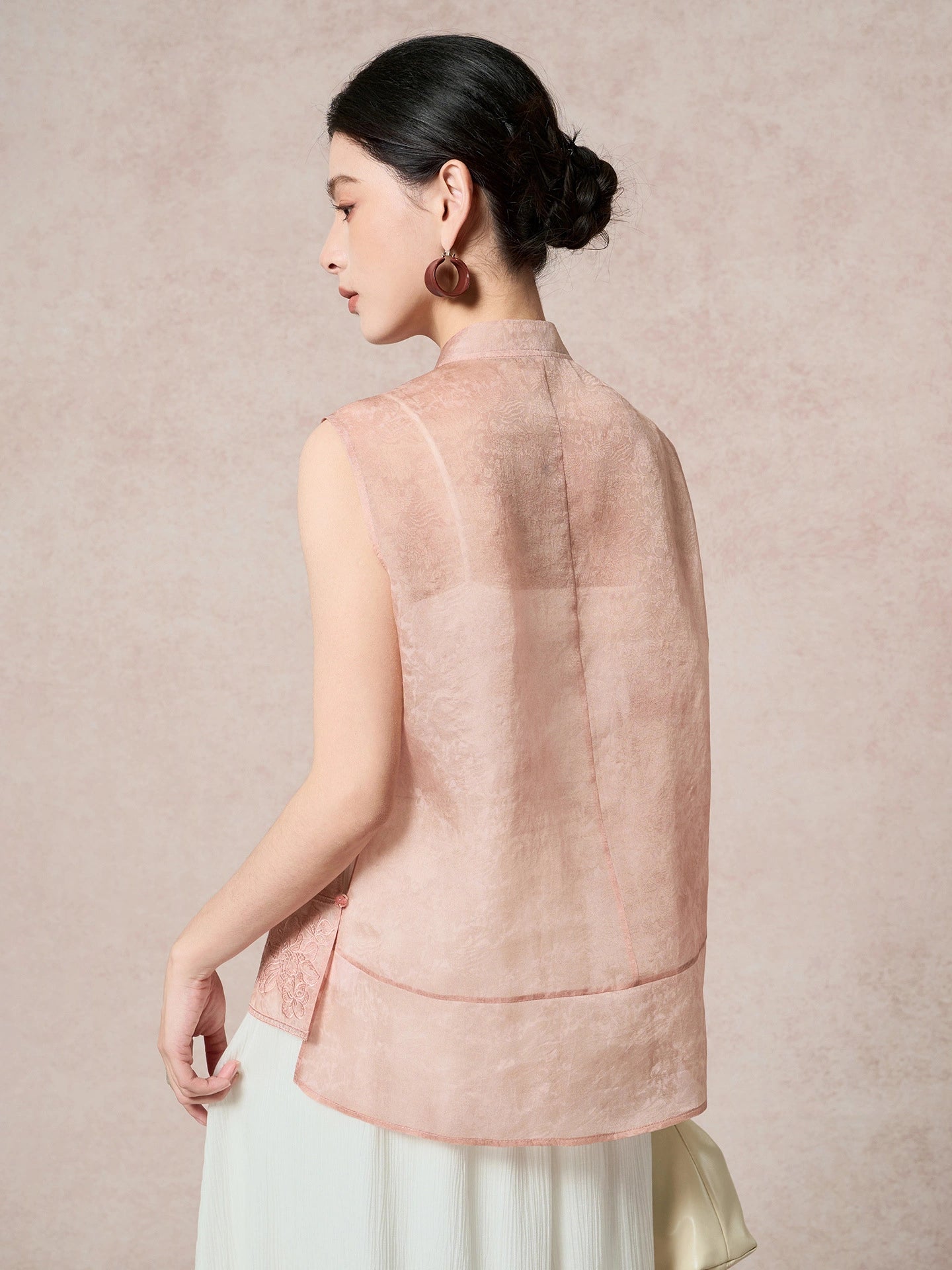 Back view of a women's pink 100% mulberry silk vest with a stand collar and subtle jacquard texture, paired with a pleated skirt.