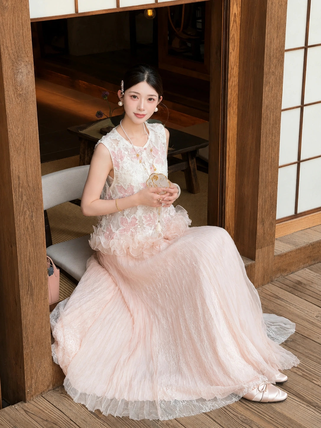 Sitting model in a pink tulle and lace maxi skirt, holding a small bag, highlighting the delicate details and comfortable fit of the 100% polyester fabric.