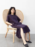 Seated model wearing a purple crackle-texture mulberry silk qipao-inspired dress with Chinese button details.