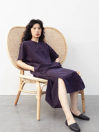 Seated model wearing a purple crackle-texture mulberry silk qipao-inspired dress with Chinese button details.