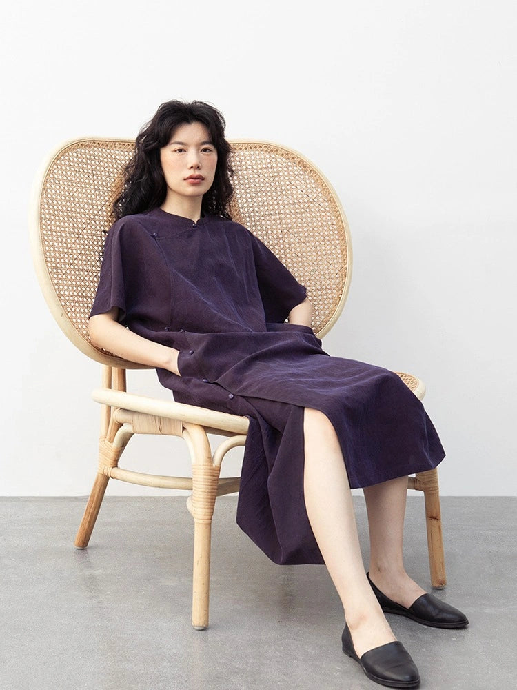 Seated model wearing a purple crackle-texture mulberry silk qipao-inspired dress with Chinese button details.