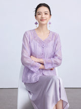 Seated model in a purple V-neck cardigan with intricate butterfly embroidery and front buttons, styled with a matching satin skirt.