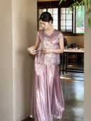 Side view of a purple shiny pleated skirt styled with a textured top, adjusting the side tie detail, crafted from 100% polyester.