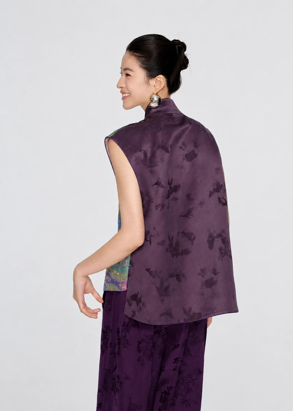 Back three-quarter view of a woman wearing the purple mulberry silk Shu brocade vest with subtle tonal jacquard motifs.