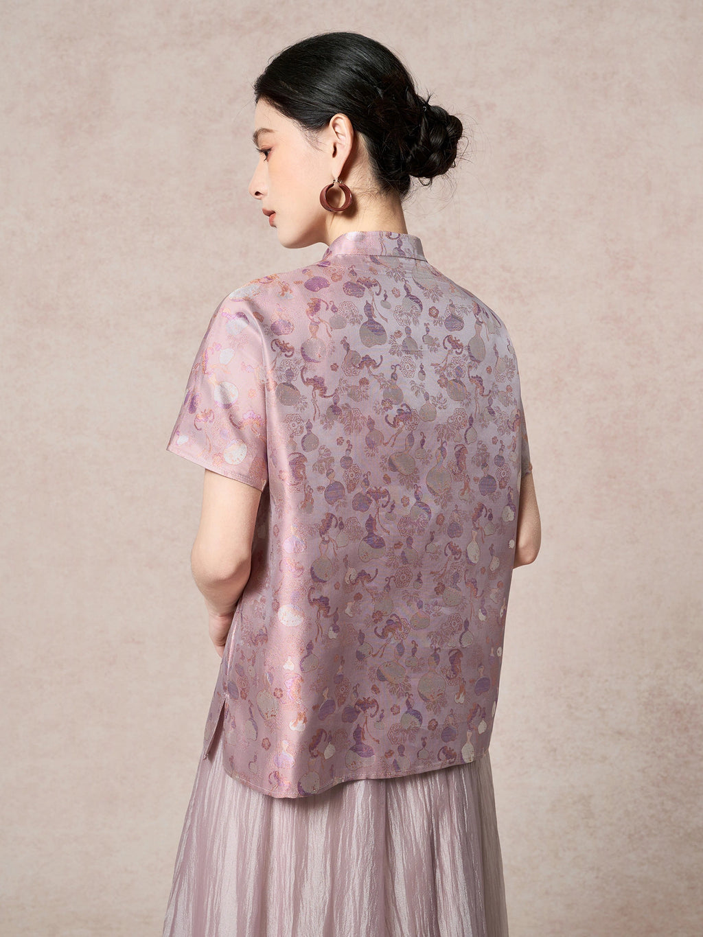 Back view of a purple silk Cheongsam top showcasing the intricate floral jacquard pattern and relaxed silhouette, paired with a pleated skirt.