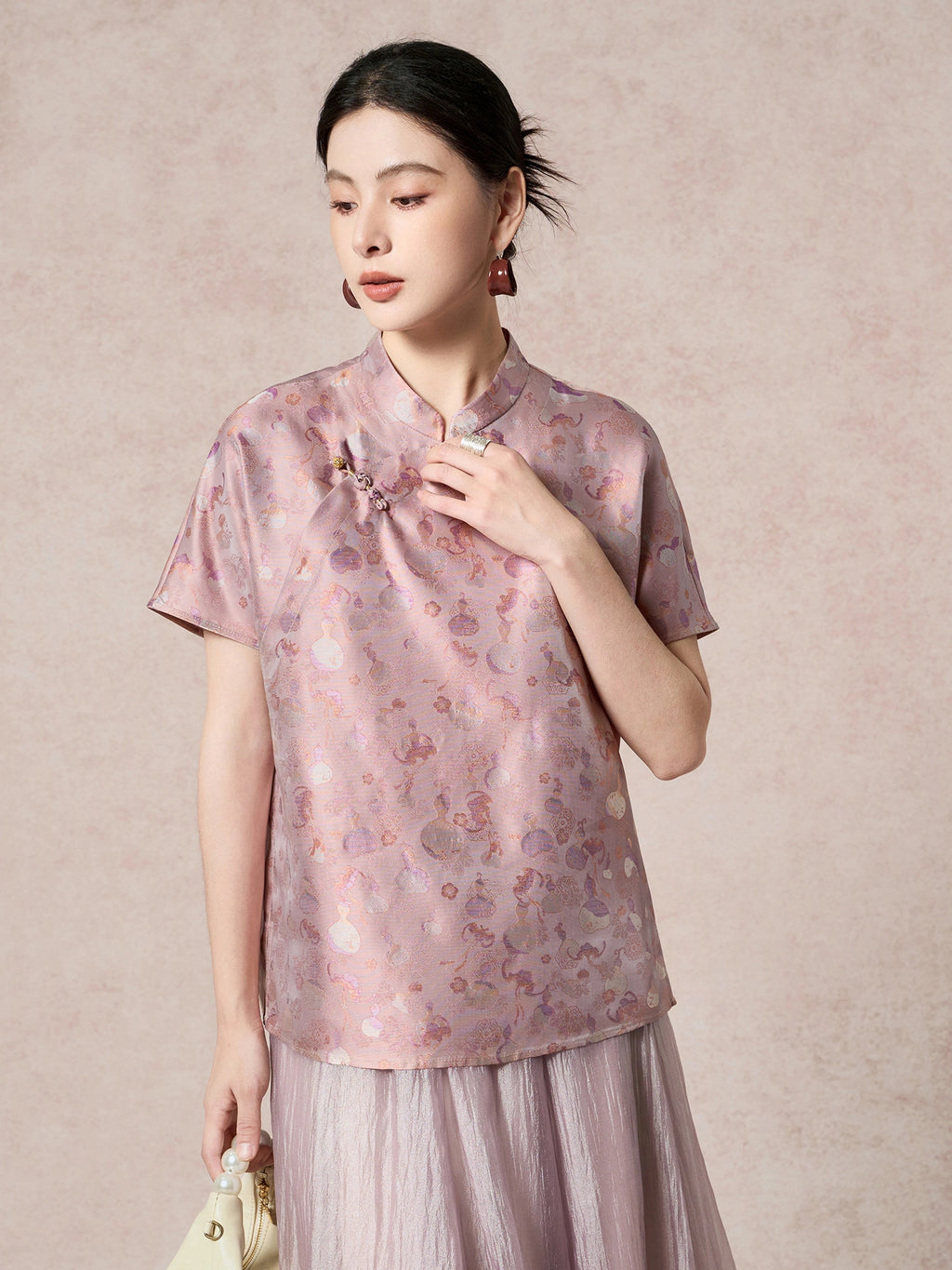 Front view of a women's purple silk top with a stand collar, short sleeves, and intricate jacquard pattern, styled with a matching pleated skirt.