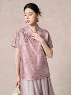 Front view of a women's purple silk top with a stand collar, short sleeves, and intricate jacquard pattern, styled with a matching pleated skirt.