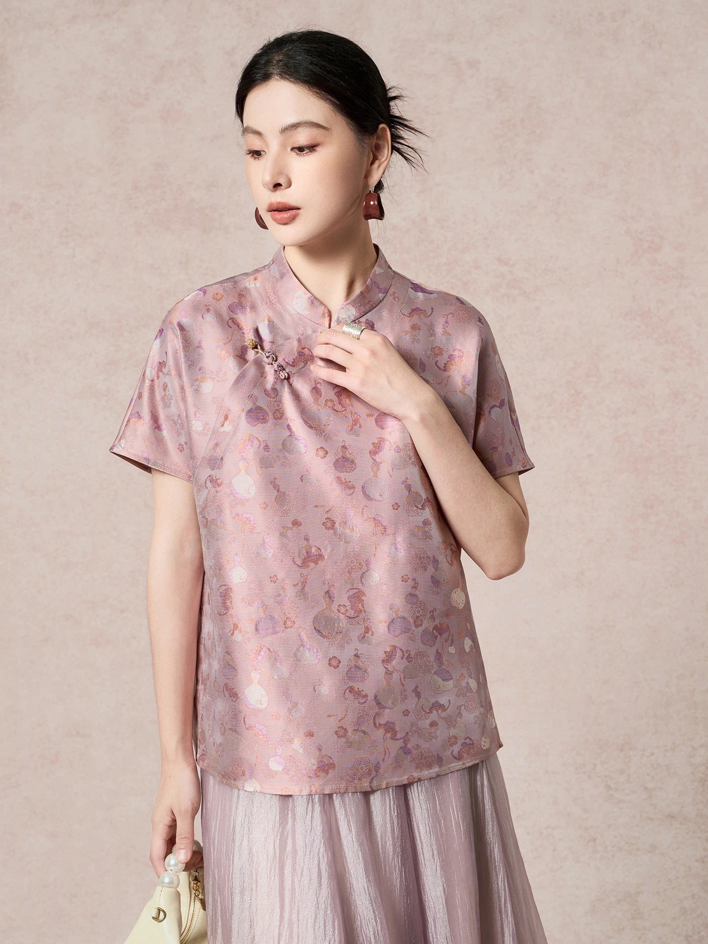 Front view of a women's purple silk top with a stand collar, short sleeves, and intricate jacquard pattern, styled with a matching pleated skirt.