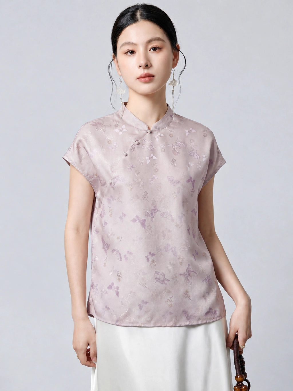 Model wearing a light purple 94% mulberry silk top with a stand collar, asymmetrical button placket, and butterfly jacquard pattern, paired with a white skirt.