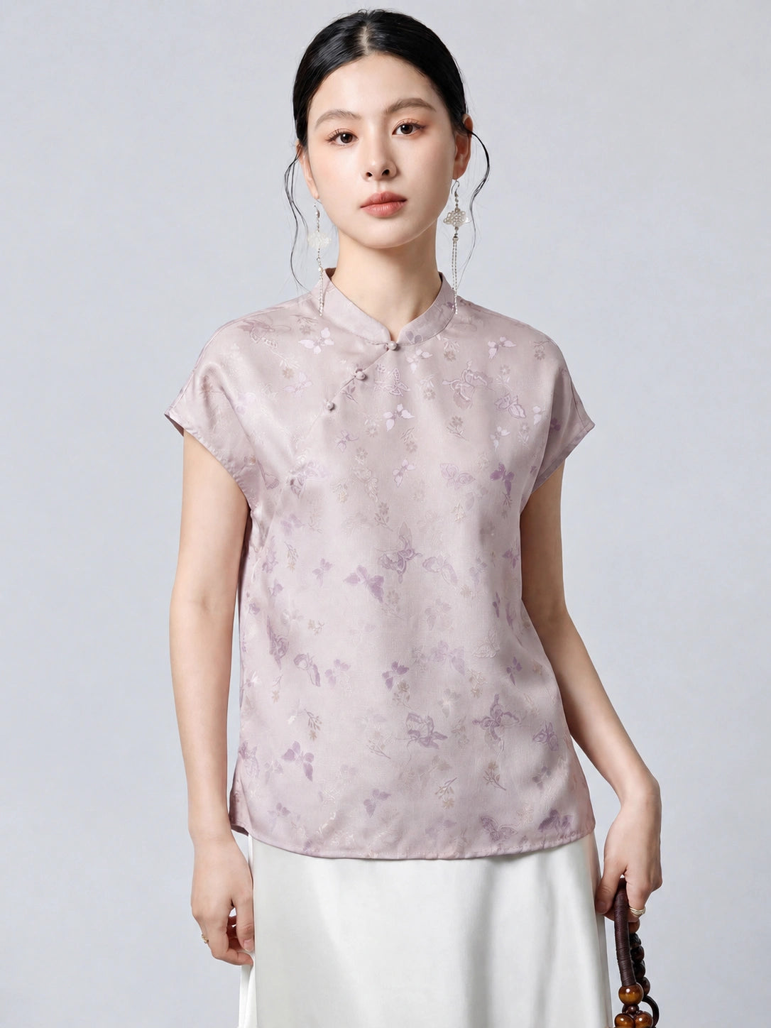 Model wearing a light purple 94% mulberry silk top with a stand collar, asymmetrical button placket, and butterfly jacquard pattern, paired with a white skirt.