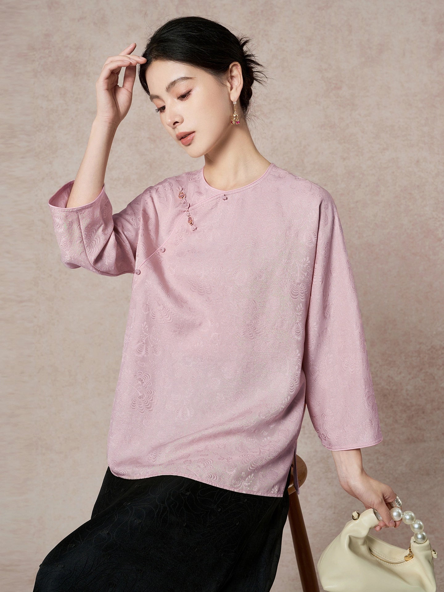 Model wearing a purple 19-momme mulberry silk blouse with a round neck, decorative buttons, and side slits, paired with a black skirt and a cream handbag.