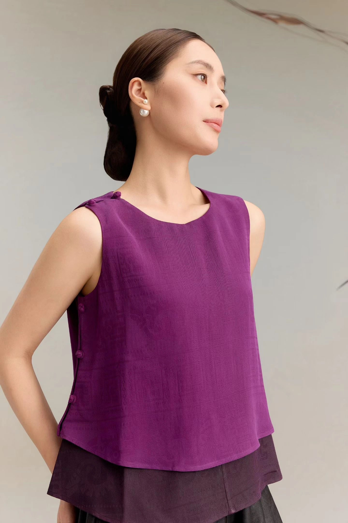 Side view of a purple silk sleeveless top with a layered hem and side button details, showcasing the elegant drape and the round neckline of the 100% silk blouse.