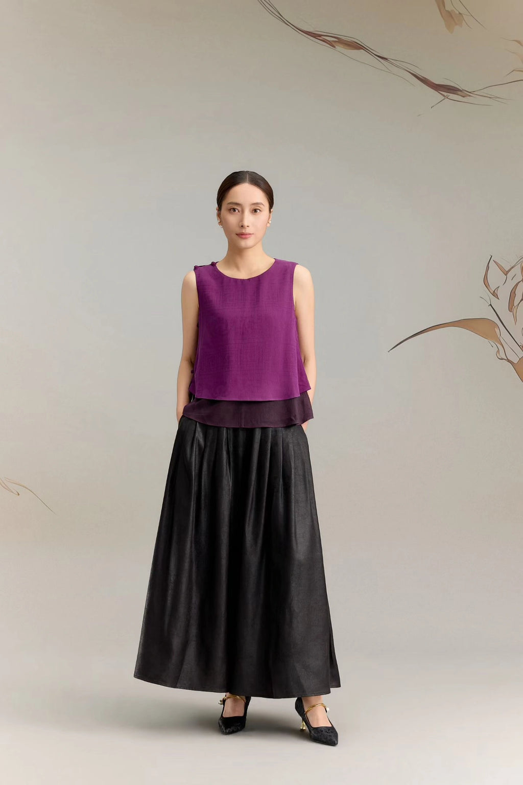 Full body shot of a purple silk sleeveless tank top with a layered hem design, paired with a black pleated maxi skirt, crafted from 100% mulberry silk.
