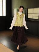 Woman wearing a green floral Song brocade silk vest over a white blouse and dark skirt