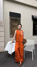 Model in a burnt orange sleeveless Cheongsam top with white floral embroidery, paired with matching wide-leg trousers.