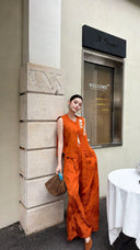Full body shot of a rust orange co-ord set, featuring a mandarin collar vest and palazzo pants, styled with a woven bag.
