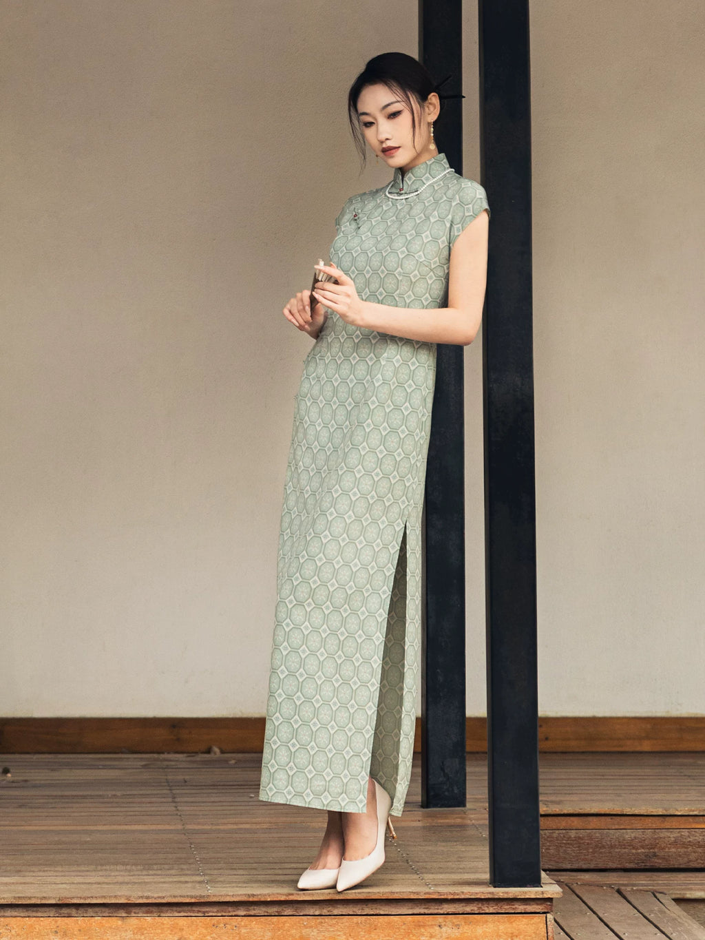 Woman wearing a sage green jacquard cheongsam dress in a minimalist architectural setting.