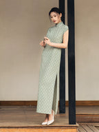 Woman wearing a sage green jacquard cheongsam dress in a minimalist architectural setting.
