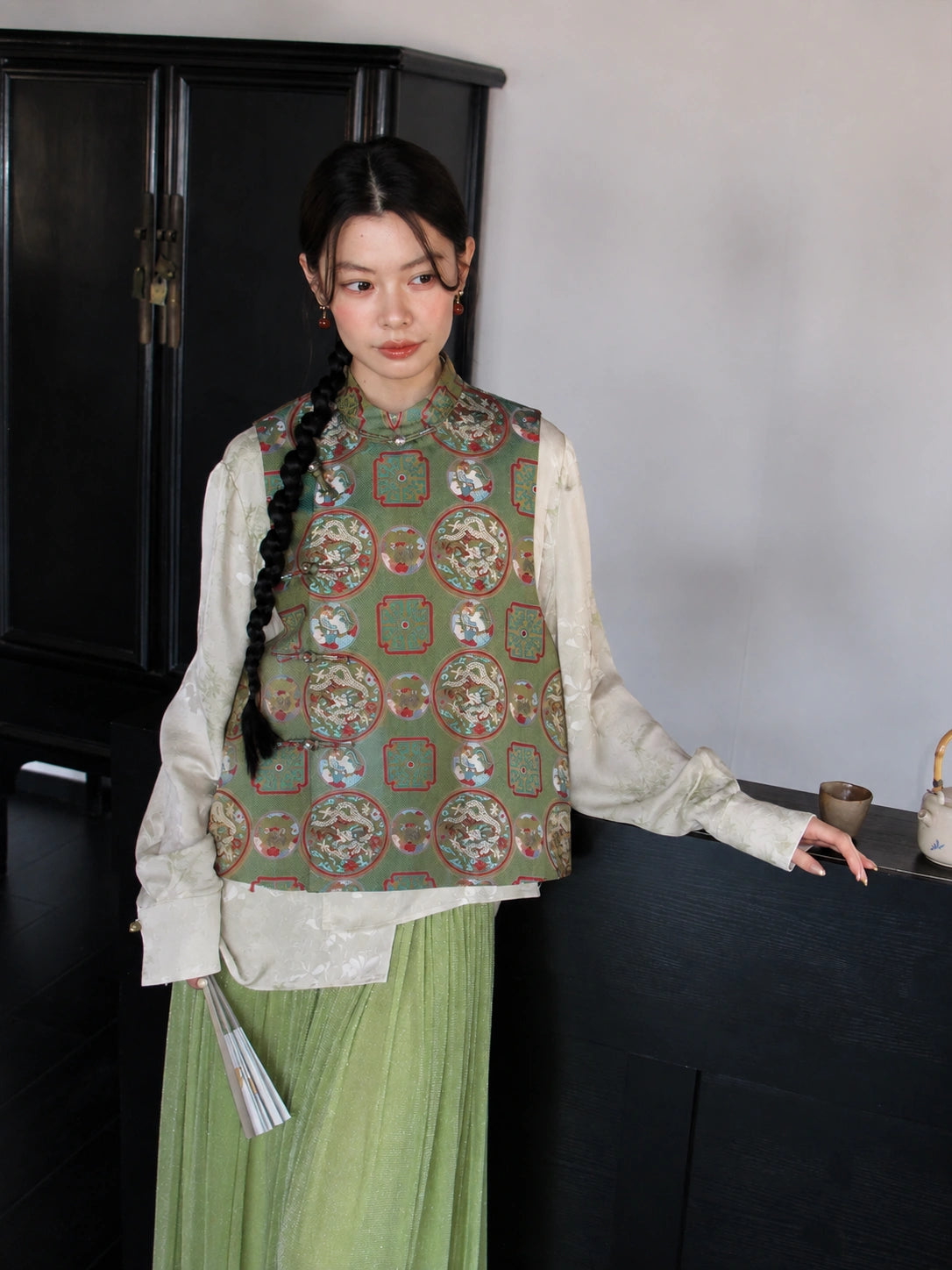 Front view of a sage green Chinese-style silk vest featuring a stand collar and traditional dragon and phoenix motifs.