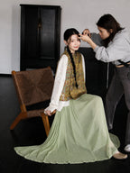 Seated styling of a 100% mulberry silk Chinese vest with dragon and phoenix patterns and a flowing sage green skirt.