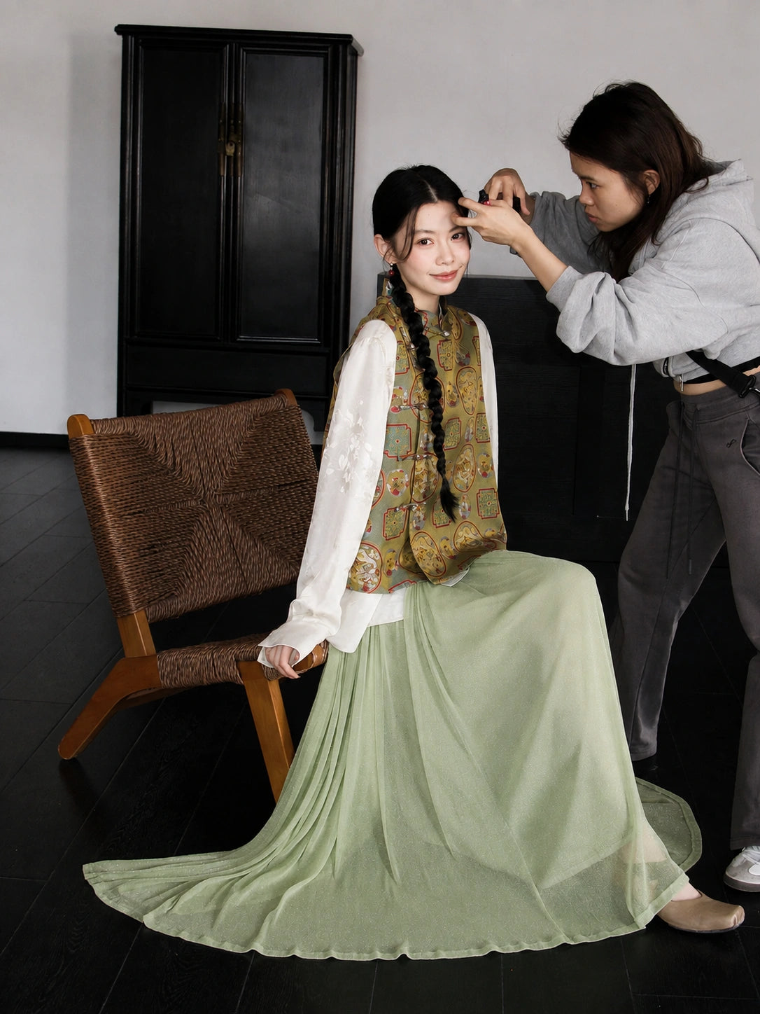 Seated styling of a 100% mulberry silk Chinese vest with dragon and phoenix patterns and a flowing sage green skirt.
