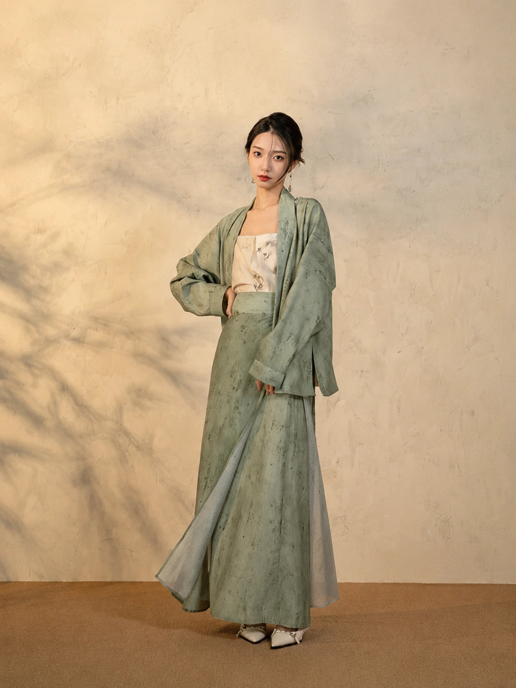 Model wearing the Sage Green Draped Sleeve Jacket and Wrap Skirt Set by Gambiered Silk.