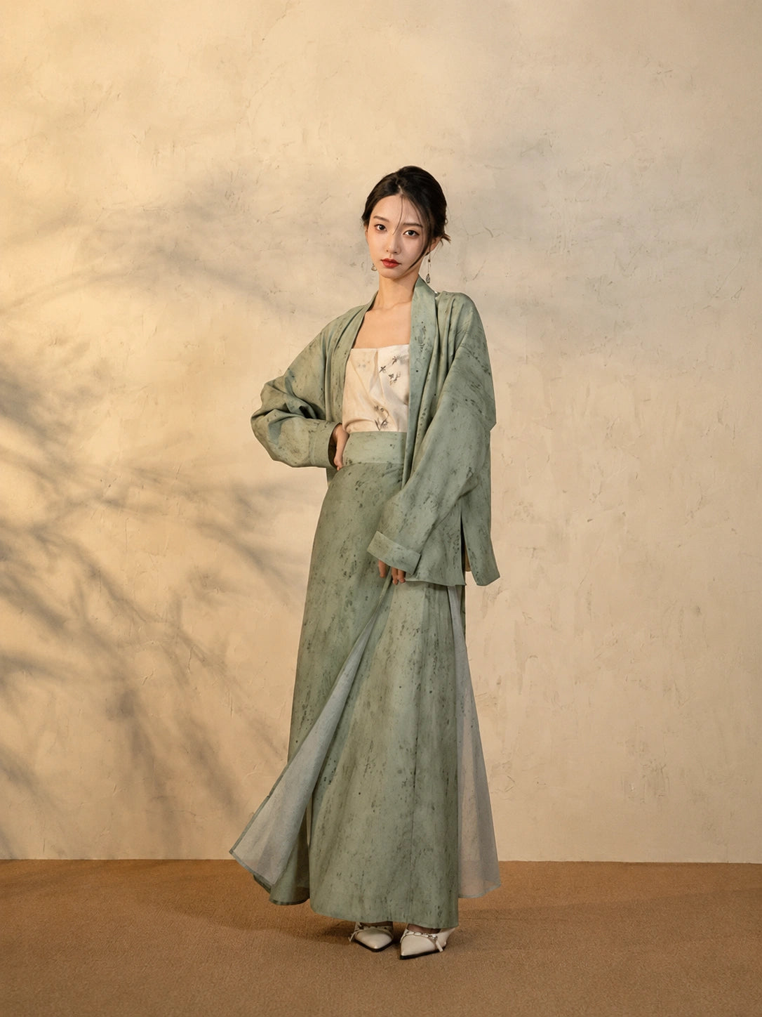 Model wearing the Sage Green Draped Sleeve Jacket and Wrap Skirt Set by Gambiered Silk.