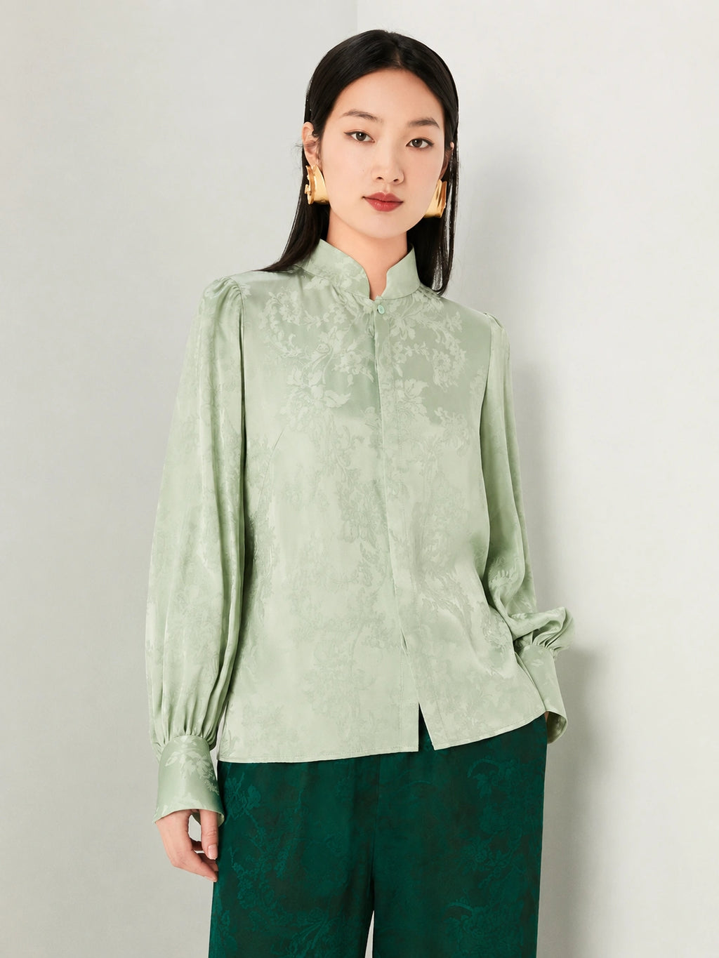 Detailed view of the floral jacquard texture on a sage green blouse.