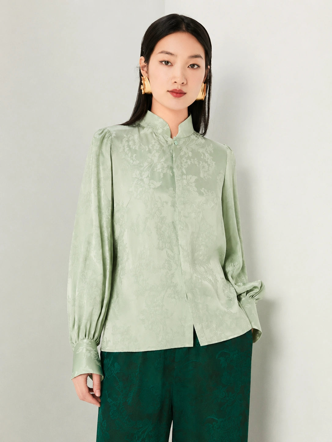 Detailed view of the floral jacquard texture on a sage green blouse.