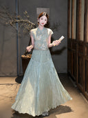 Model wearing a sage green pleated maxi skirt with a matching embroidered top and fan, showcasing the flowy drape of the 80% Lyocell, 20% Polyester blend.